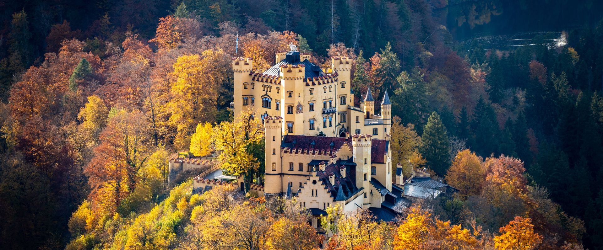 Autumnal aerial view of Hohenschwangau Castle, surrounded by colourful deciduous forest.