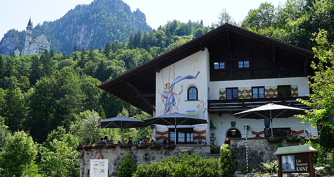 Image of the Café Kainz restaurant building with terrace and Neuschwanstein Castle in the background