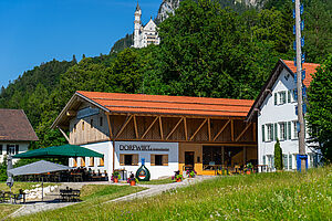 Exterior view of the Dorfwirt restaurant with terrace and Neuschwanstein Castle in the background
